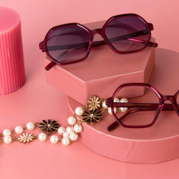 A candle, two pairs of glasses, and a necklace on a pink background